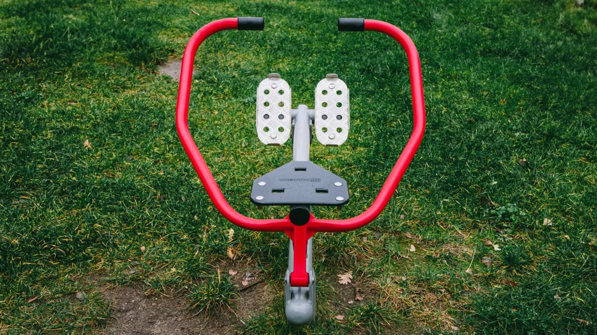 A vibrant red exercise device in a Polish park's green outdoor setting.